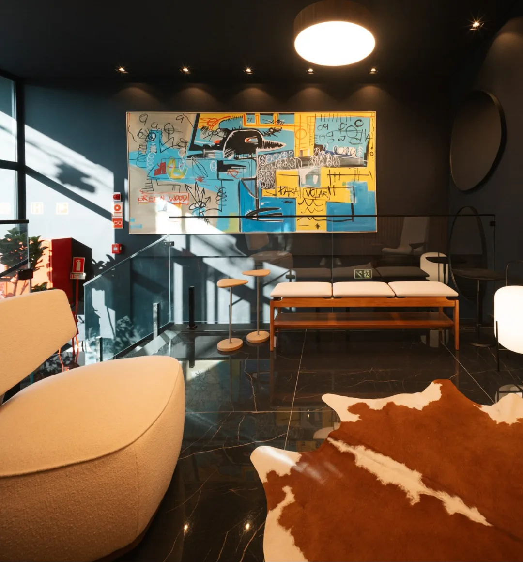 Ambiente com poltrona em bouclé, banco de madeira com assentos claros, tapete de couro e quadro colorido, mobiliado pela Hodierno